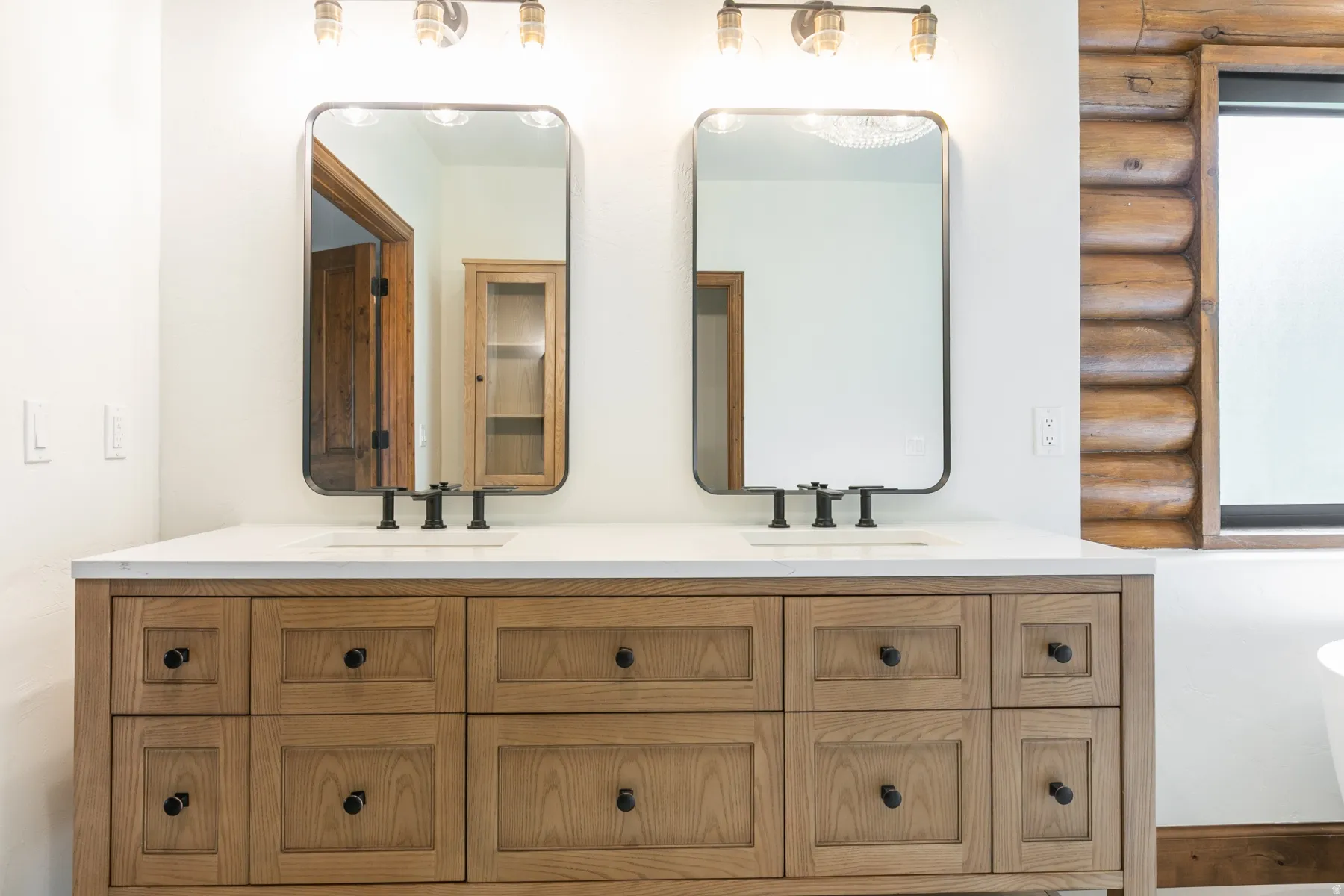 Dual vanity featuring a light wood-finish base with black hardware, white countertop, and integrated sinks