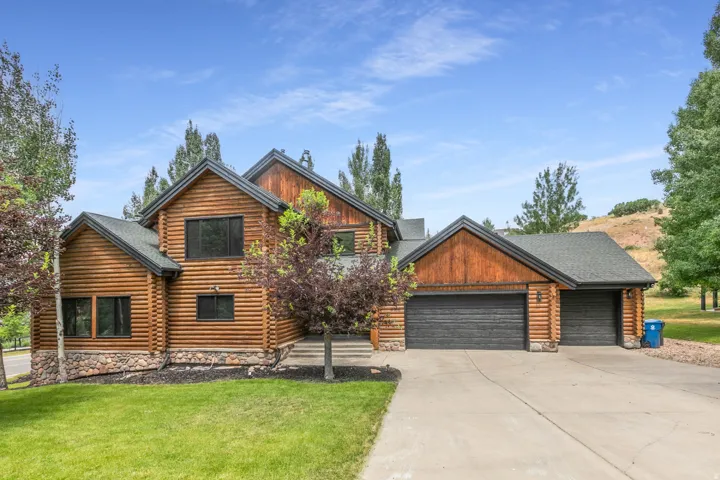 Rustic log-style home featuring a multi-gable roofline, stone foundation accents, a concrete driveway, and attached two-car garage
