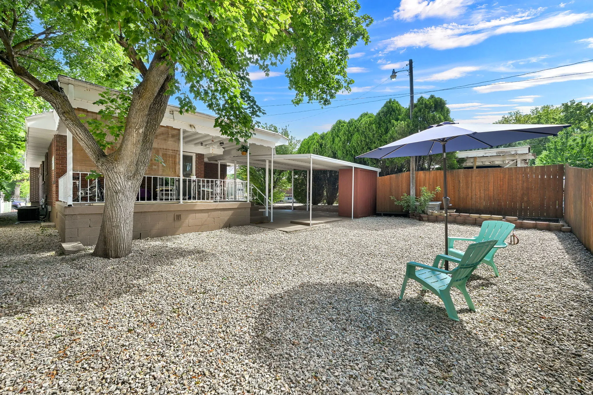 Gravel backyard featuring a privacy fence, mature trees, and a covered carport