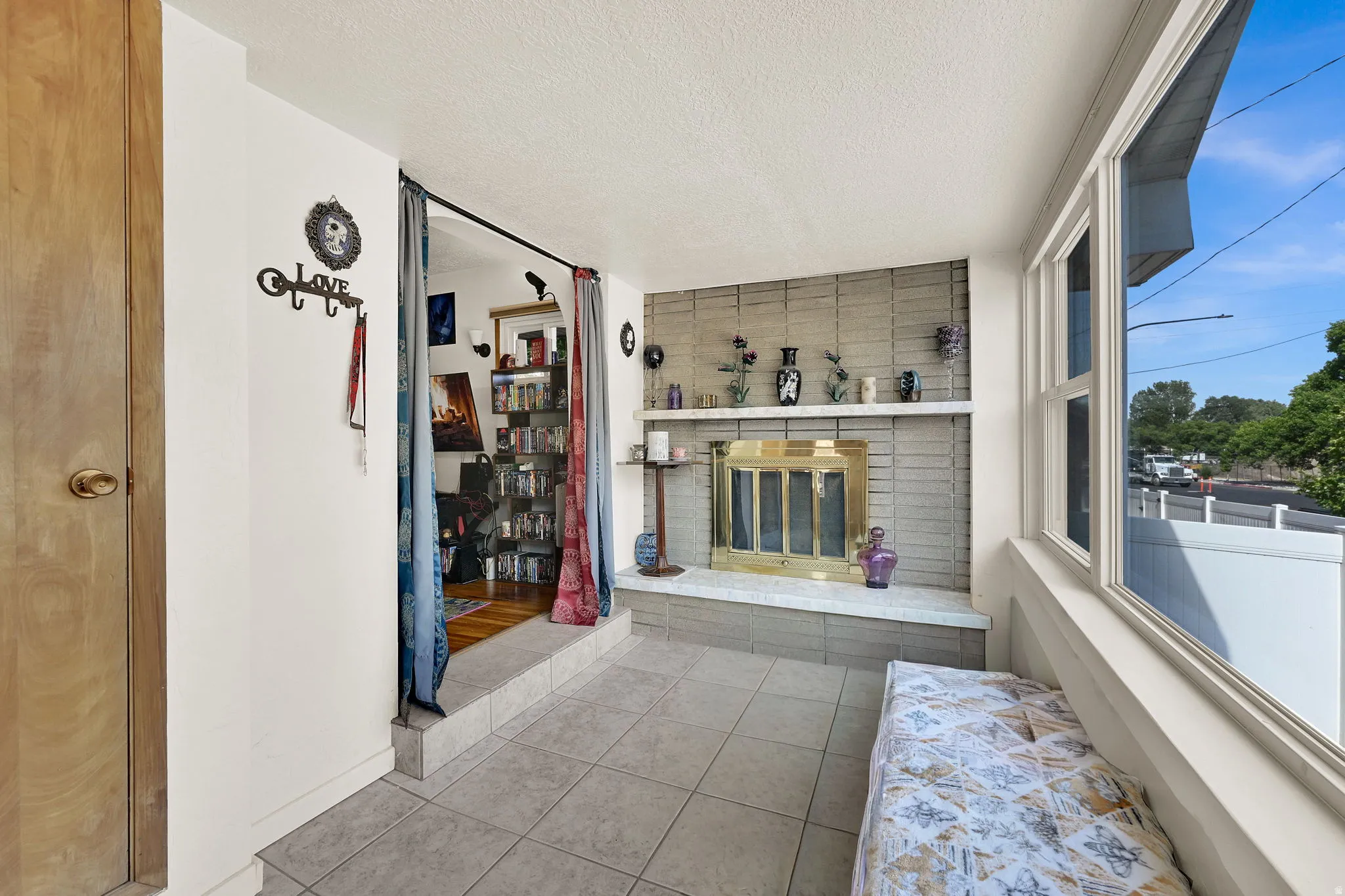 Tiled sunroom featuring large windows, a built-in fireplace with a brass-toned insert, and a white mantel