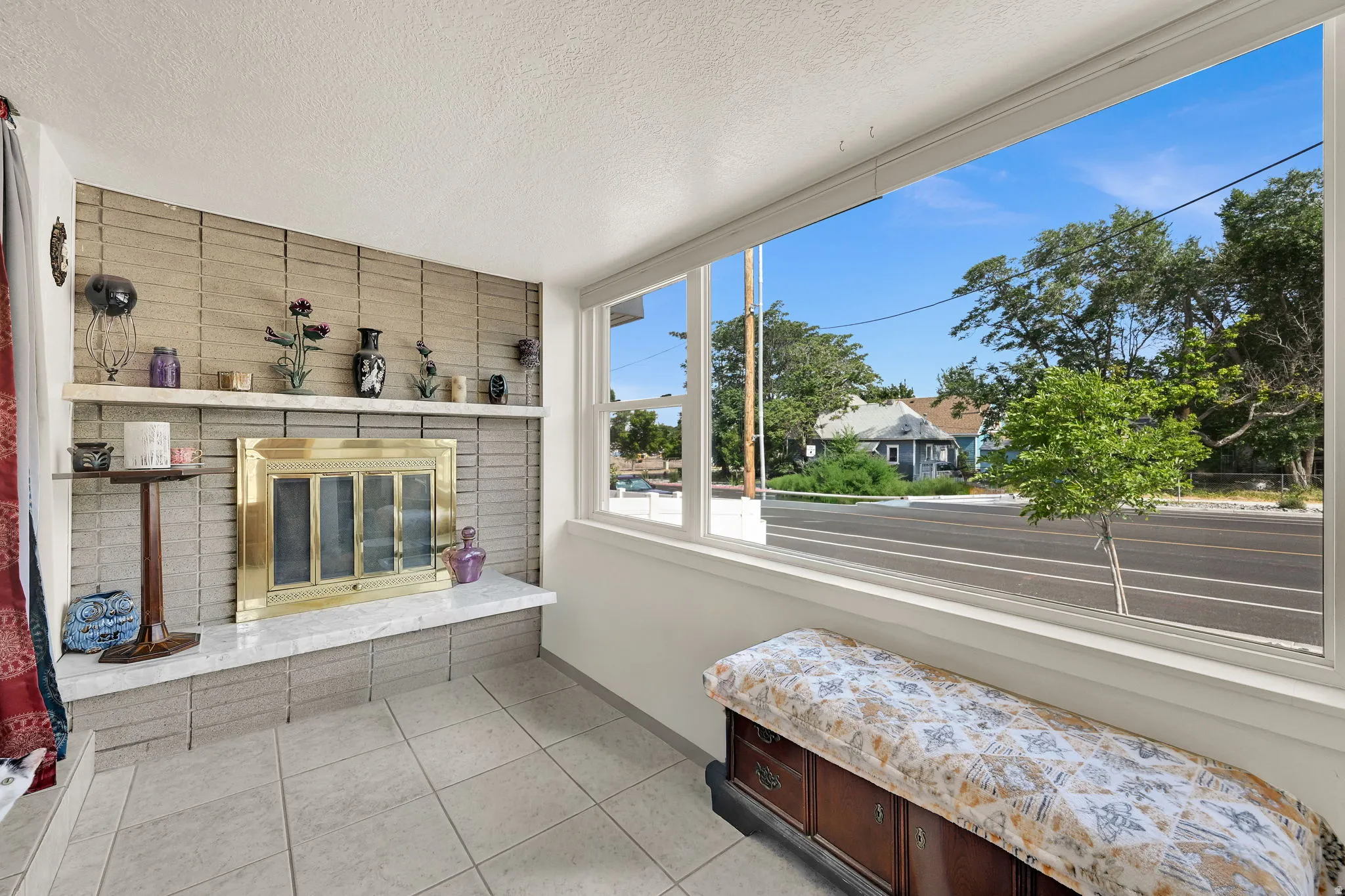 Spacious room featuring a large window, a fireplace with a brass-toned insert, a tiled hearth, and a mantelpiece