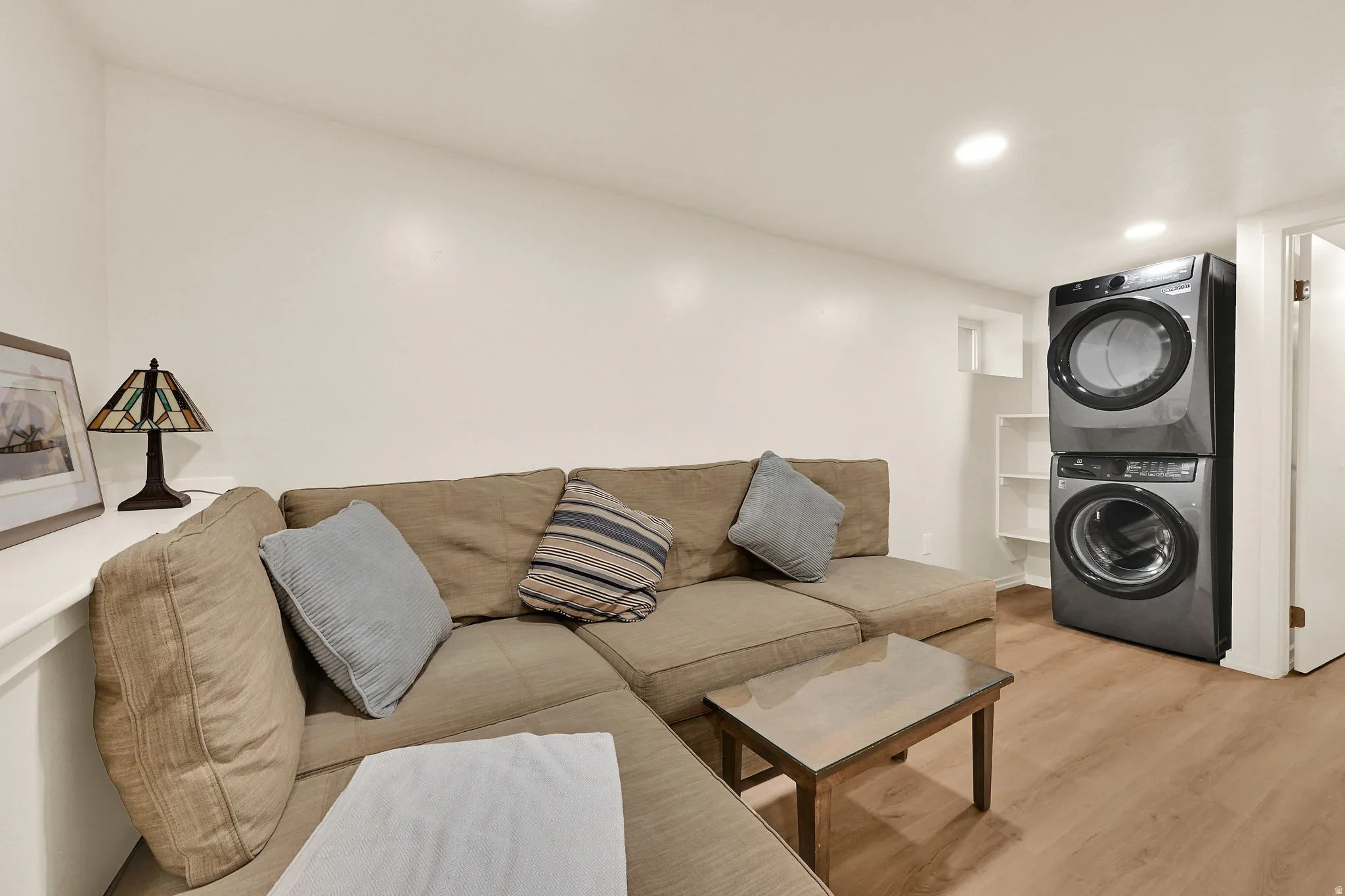 Compact laundry area featuring a stacked washer and dryer, wood-finish flooring, and recessed ceiling lighting