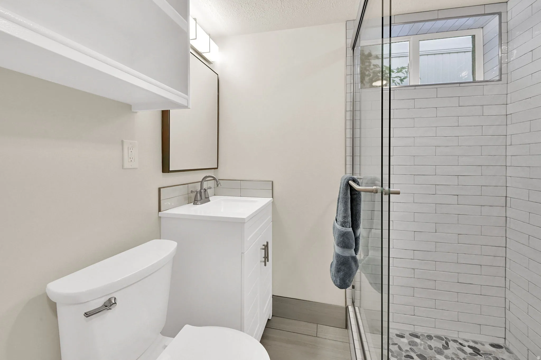 Bathroom featuring a glass-enclosed shower with pebble-finish flooring and white subway tile surround
