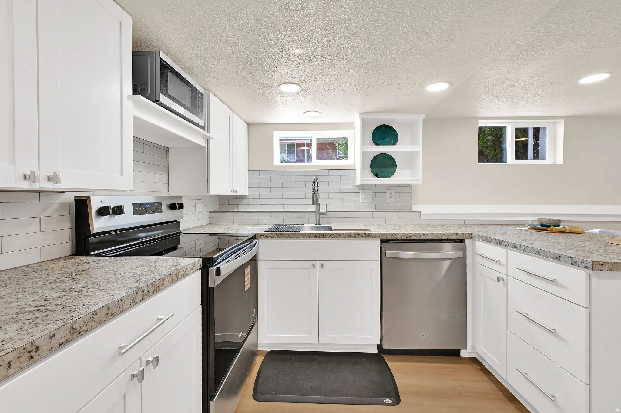 Bright kitchen featuring abundant white cabinetry, light wood-finish flooring, recessed lighting, and stainless steel appliances including a built-in microwave, range, and dishwasher