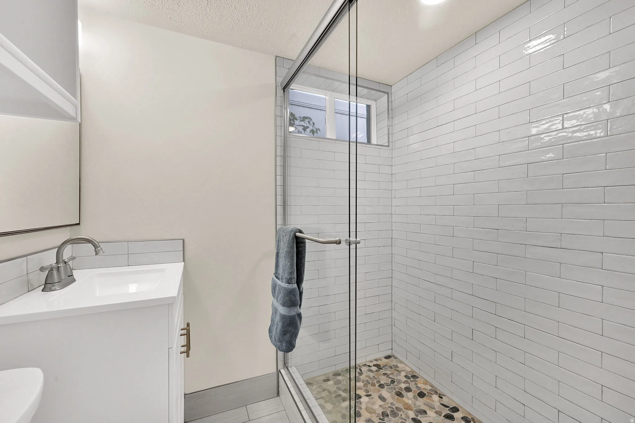 Glass-enclosed shower with white subway tile surround and a pebble stone floor