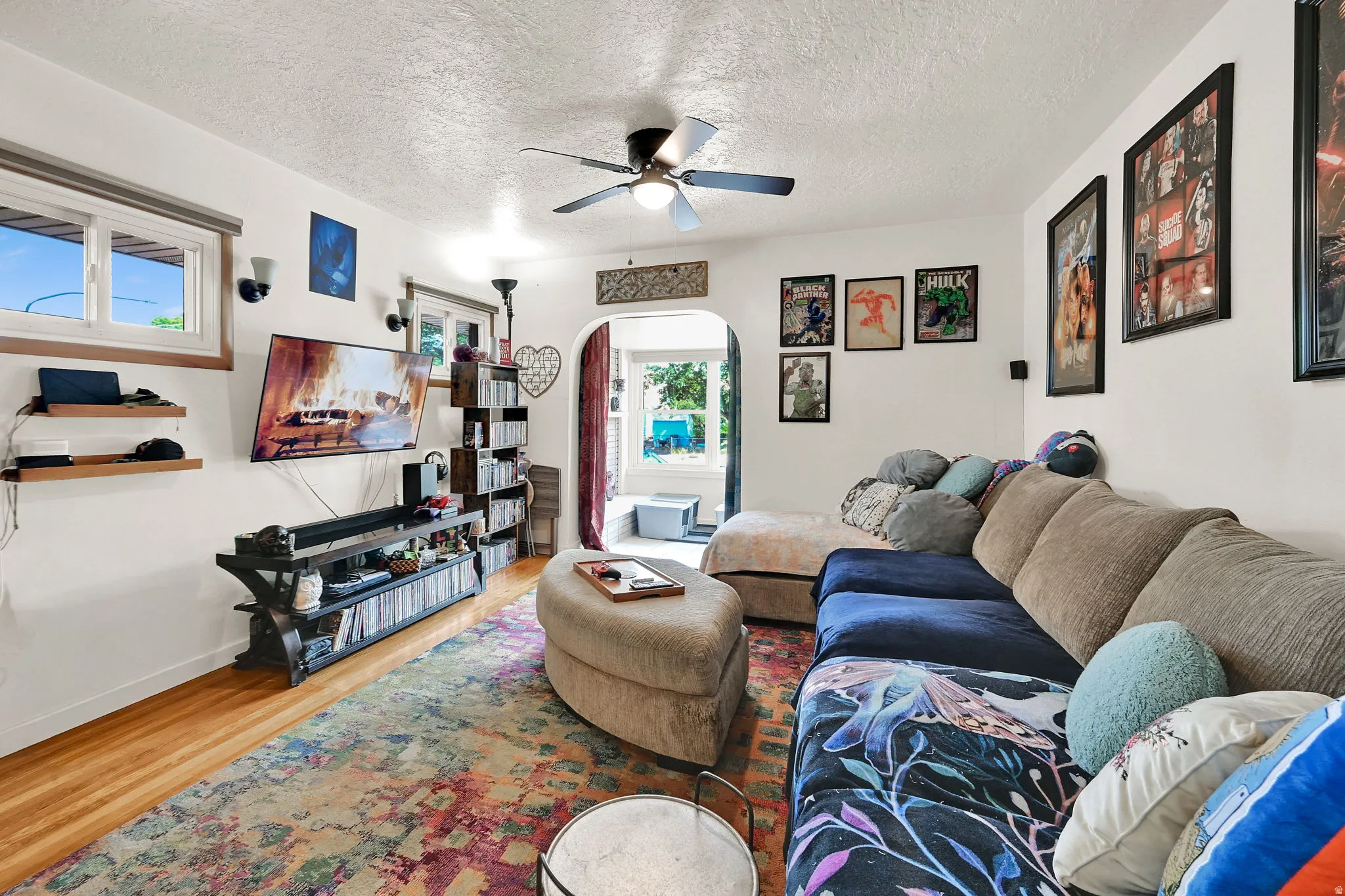 Spacious living area featuring wood-finish flooring, a ceiling fan, and multiple windows for natural illumination