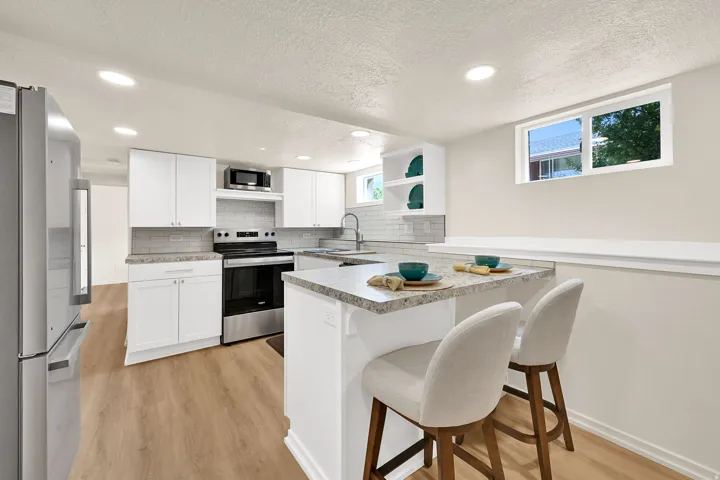 Contemporary kitchen featuring white cabinetry, stainless steel appliances, a light-toned backsplash, granite-finish countertops, and wood-finish flooring