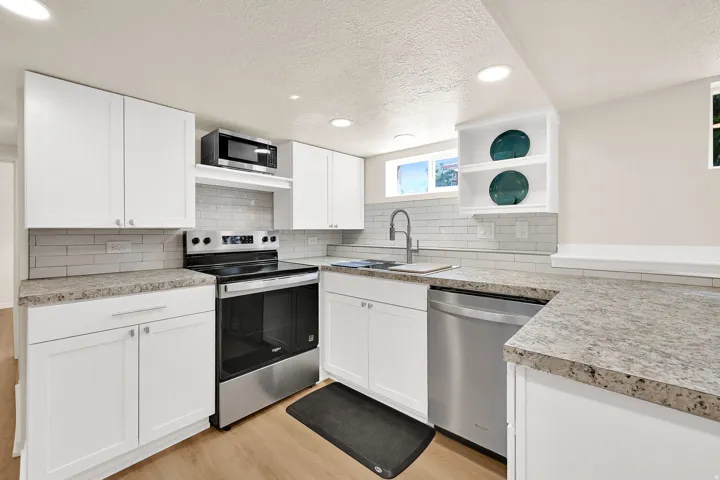 Modern kitchen featuring white shaker cabinetry, stainless steel appliances, speckled countertops, a tile backsplash, and recessed lighting