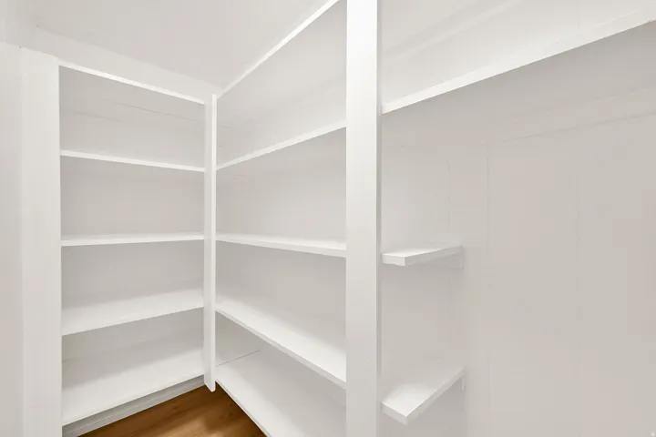 Built-in shelving system featuring multiple white shelves, a corner configuration, and wood-finish flooring