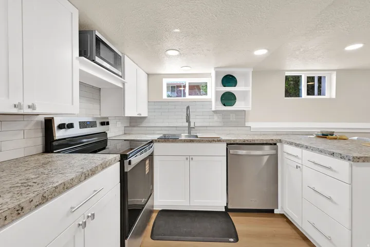 Bright kitchen featuring abundant white cabinetry, light wood-finish flooring, recessed lighting, and stainless steel appliances including a built-in microwave, range, and dishwasher