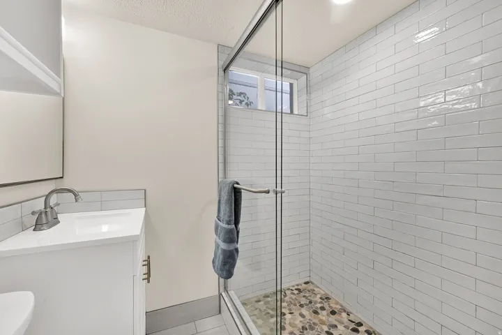 Glass-enclosed shower with white subway tile surround and a pebble stone floor