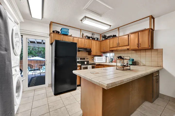 Kitchen featuring light wood cabinetry with open shelving, a tile backsplash, and a tiled countertop island