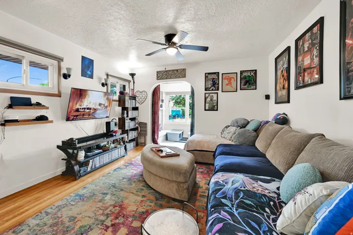 Spacious living area featuring wood-finish flooring, a ceiling fan, and multiple windows for natural illumination