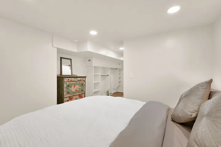 Recessed lighting illuminates a spacious room featuring a built-in closet system with open shelving and hanging space