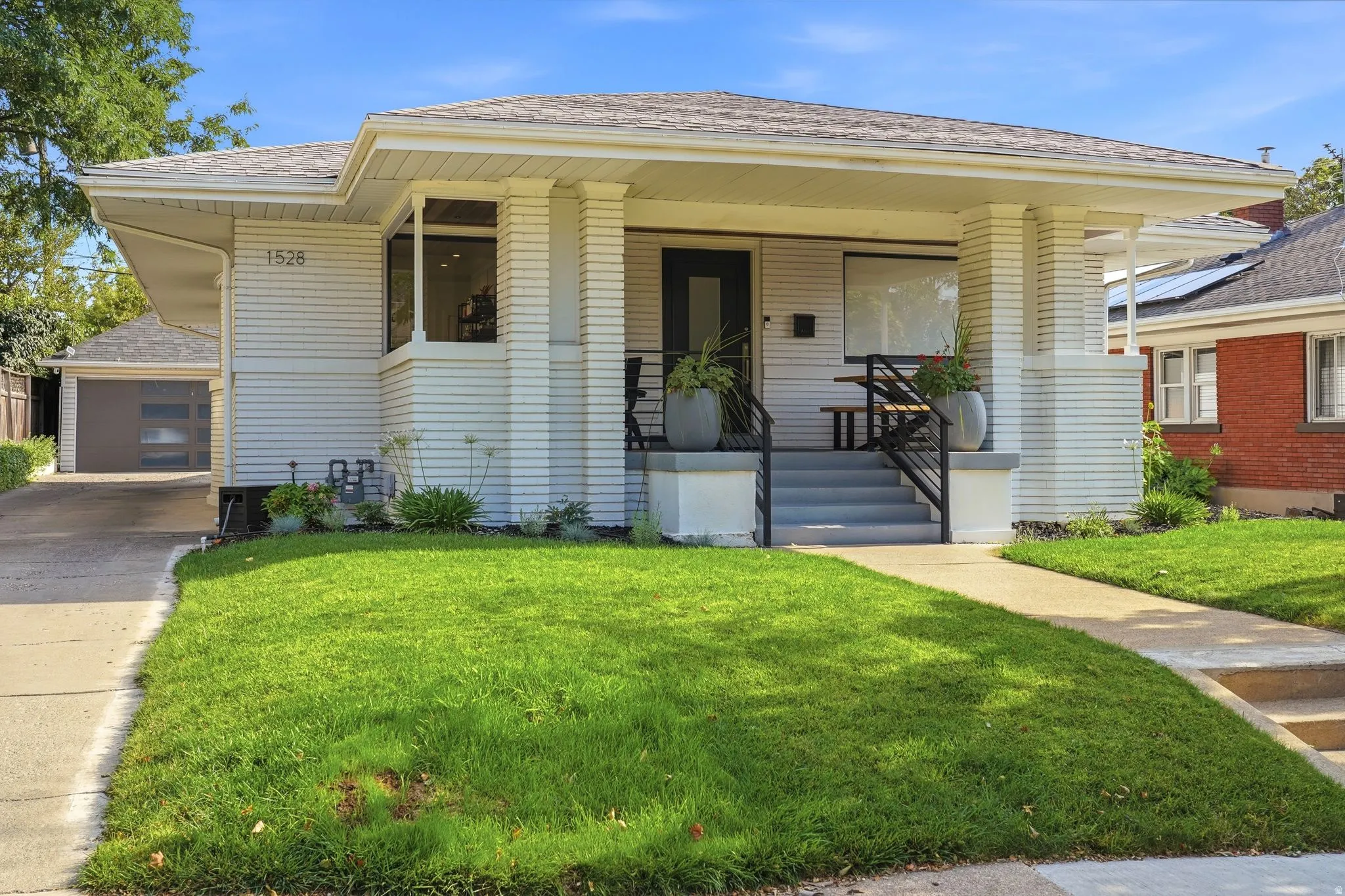 Craftsman bungalow with a covered front porch, perfectly manicured lawn, long driveway, and detached 2-car garage