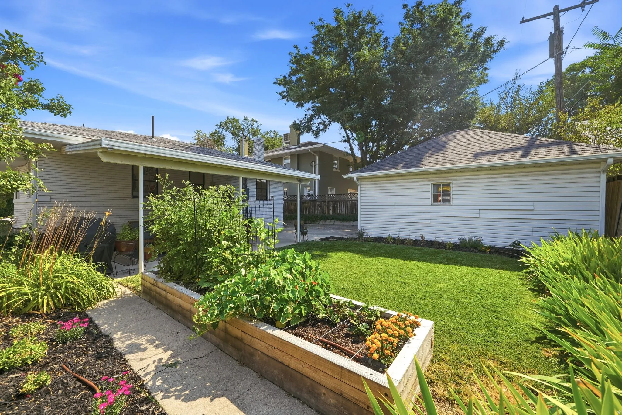 Beautiful backyard featuring a covered patio, manicured lawn, raised garden beds, 2 car garage, and fully automated sprinkler system.