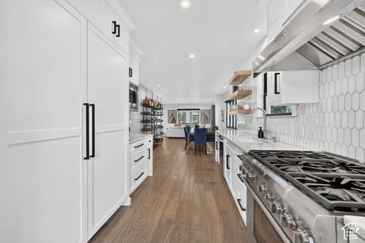 Gourmet kitchen featuring a stainless steel gas range with a professional-grade hood, tile backsplash, wood accent floating shelves, quartz countertops, and cabinet-front refrigerator & freezer