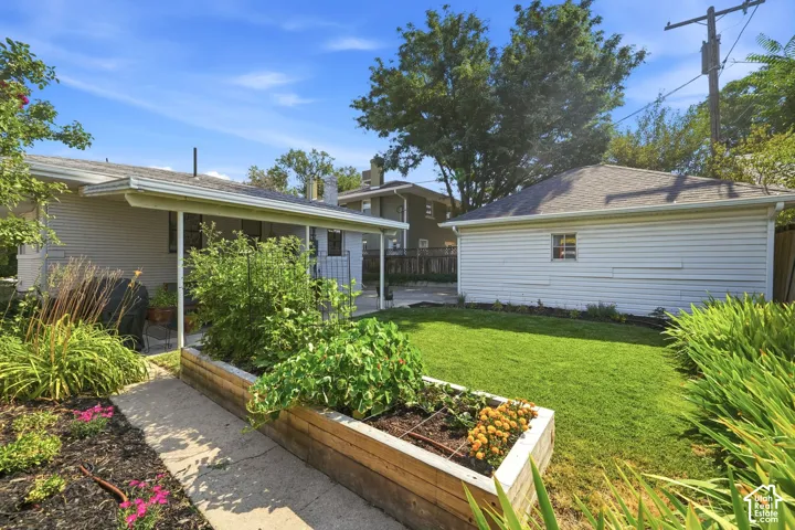 Beautiful backyard featuring a covered patio, manicured lawn, raised garden beds, 2 car garage, and fully automated sprinkler system.