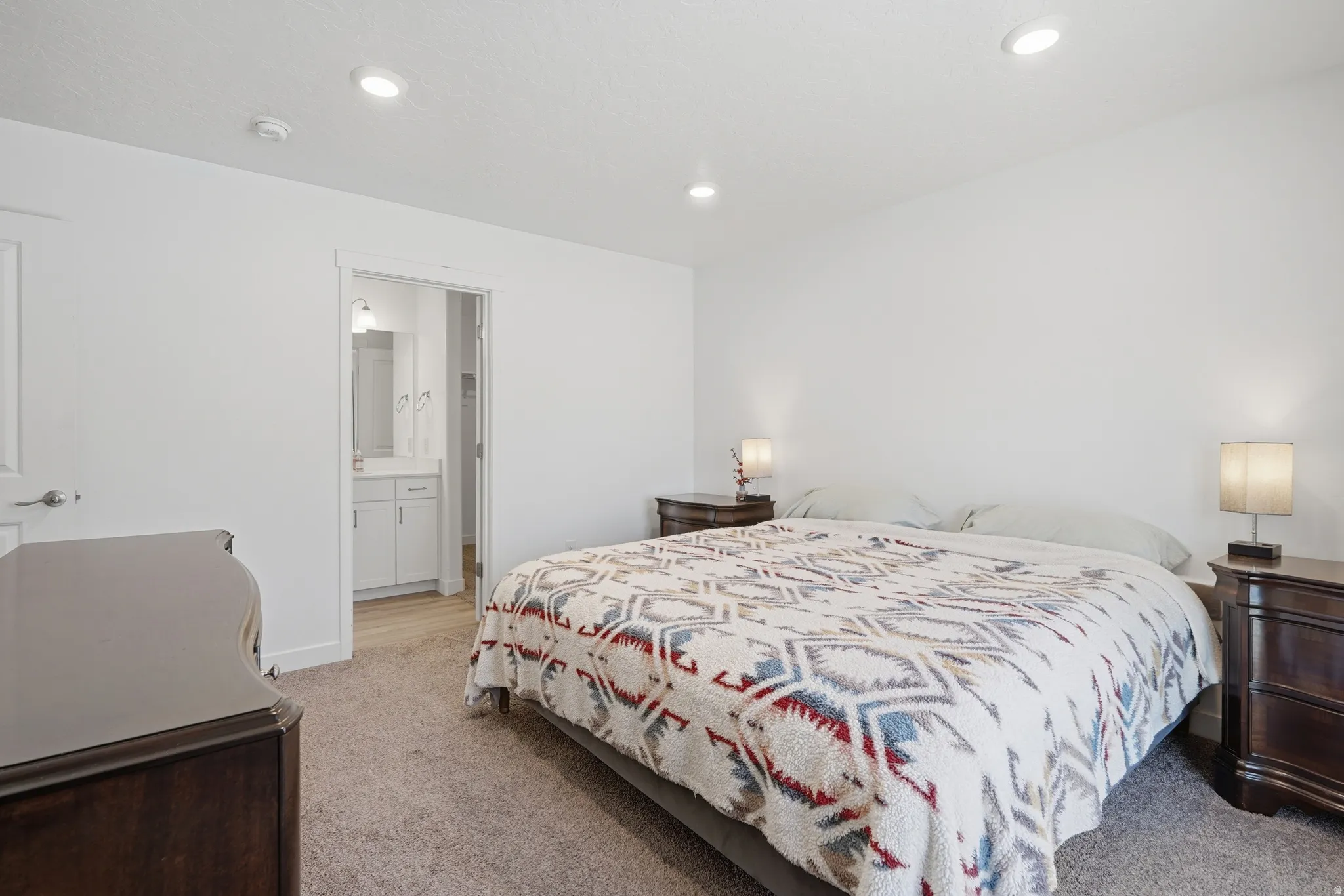 Carpeted bedroom with recessed lighting, an interior door, and a visible bathroom featuring a vanity with a sink and a mirror