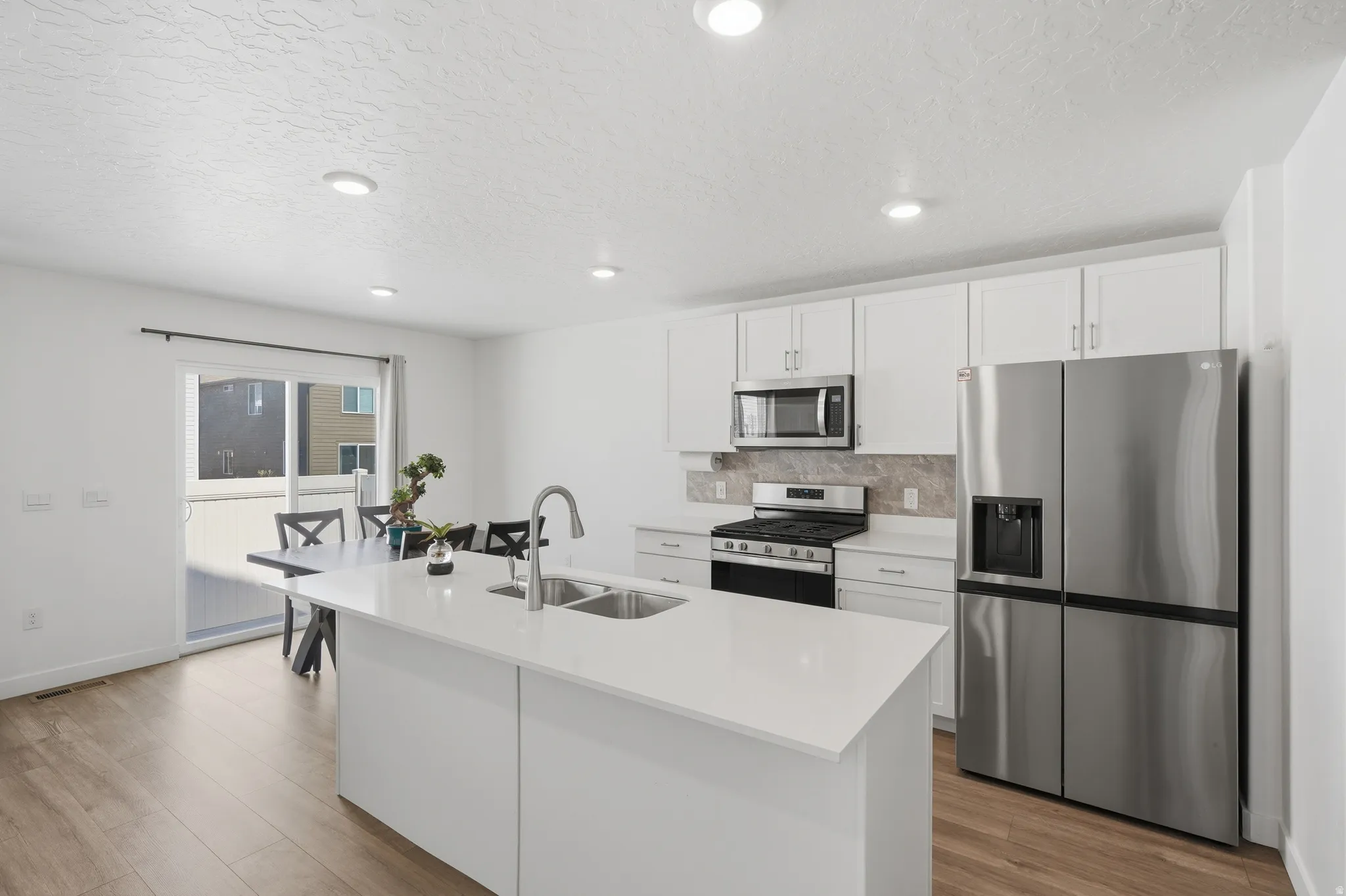Contemporary kitchen featuring white cabinetry, stainless steel appliances, a center island with double sink, and wood-finish flooring