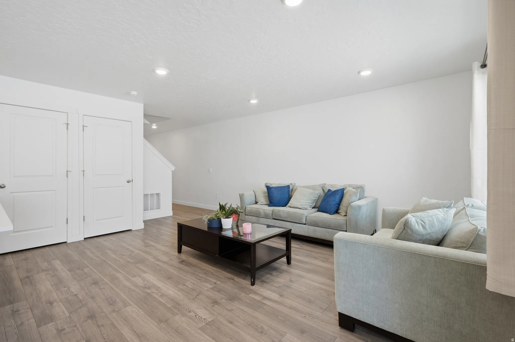 Spacious living area featuring wood-finish flooring, recessed lighting, white walls, and bright white interior doors