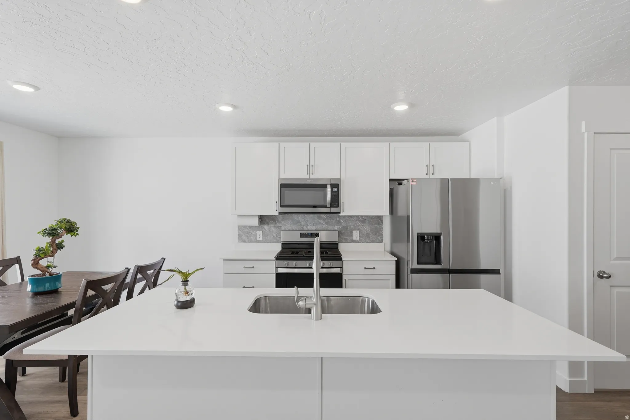 Kitchen featuring a large island with an undermount sink, white cabinetry, stainless steel appliances, and a tiled backsplash