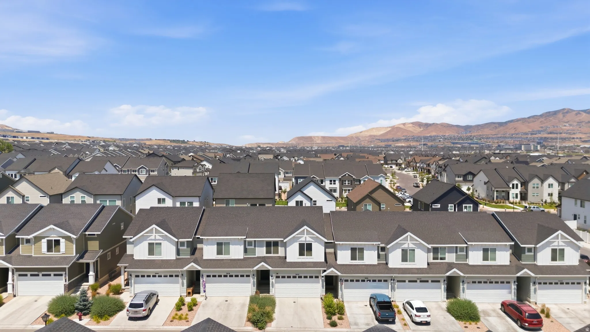 Residential street featuring two-story homes with attached garages, dark shingle roofs, and light-colored siding