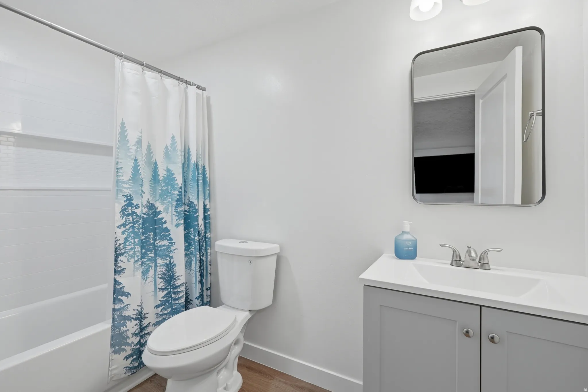 Bathroom featuring a white bathtub with subway tile surround, a toilet, and a vanity with gray cabinetry and a white countertop