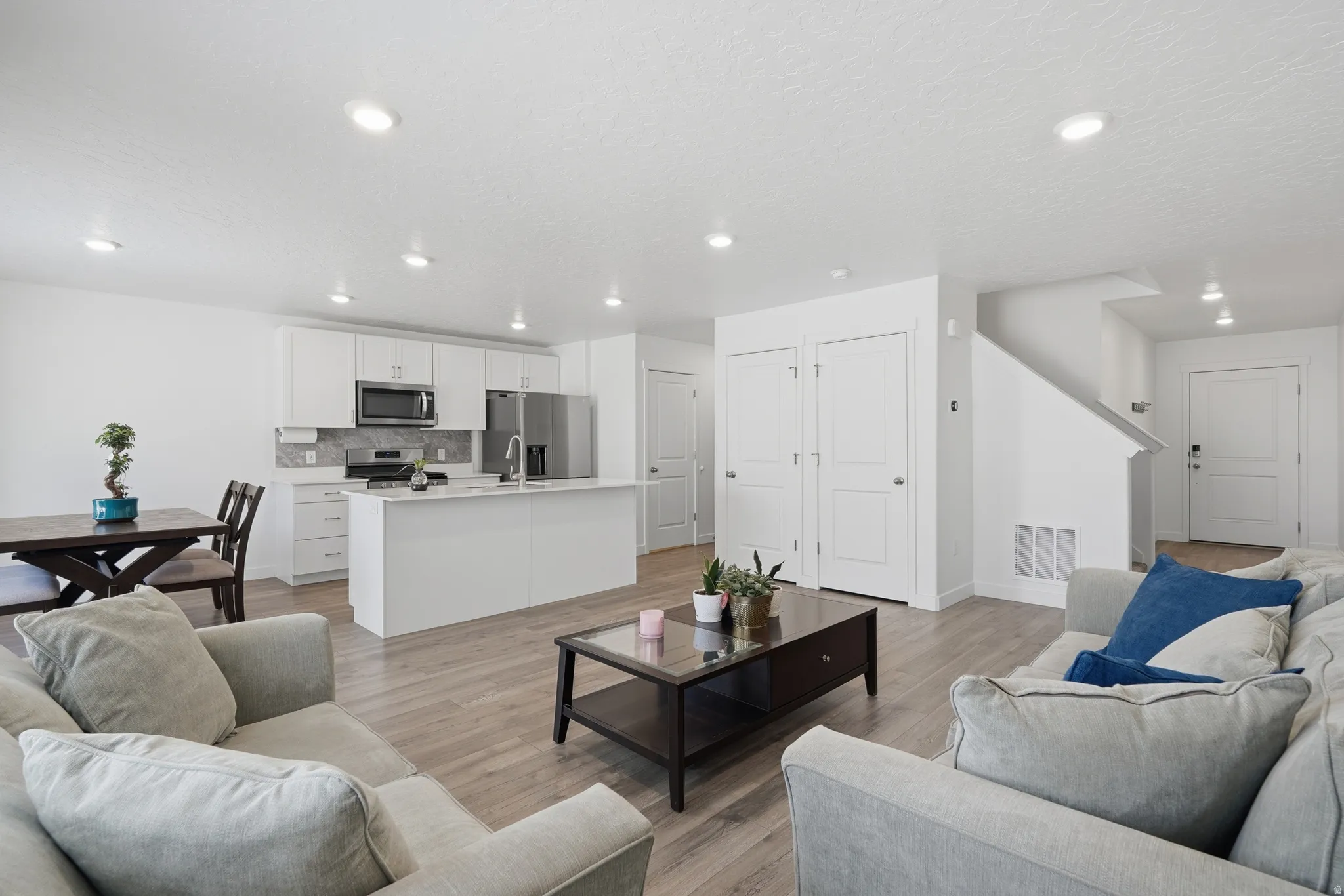 Open-concept living area featuring wood-finish flooring, recessed lighting, and a white kitchen with stainless steel appliances