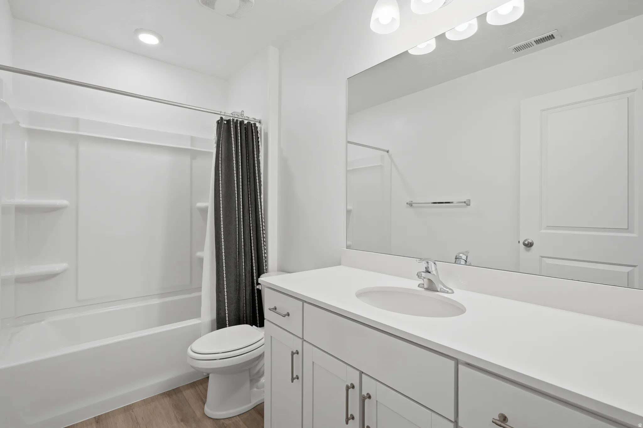Bathroom featuring a white vanity with an integrated sink, a large wall-mounted mirror, and a tub/shower combination with white surround