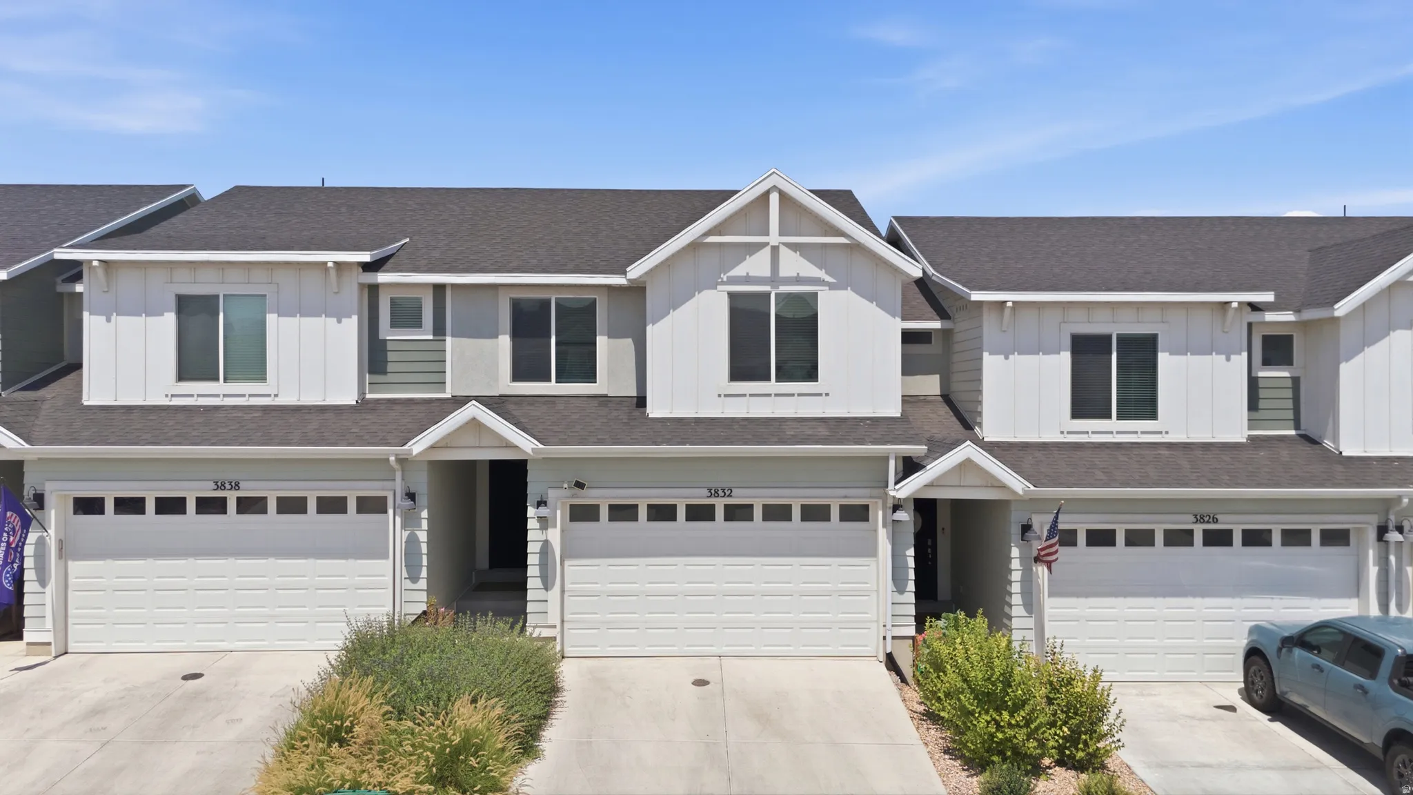 Contemporary townhome exterior featuring light-colored siding, dark shingle roofing, and integrated single-car garages