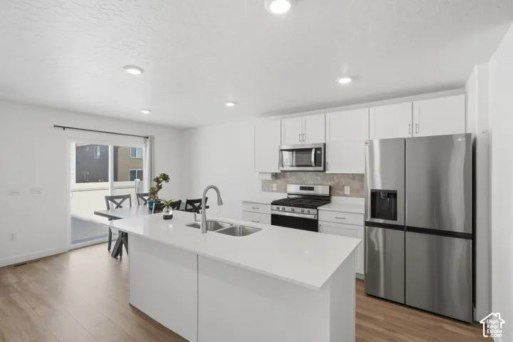 Contemporary kitchen featuring white cabinetry, stainless steel appliances, a center island with double sink, and wood-finish flooring