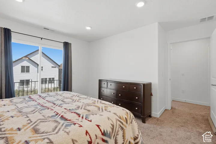 Bright bedroom featuring a sliding glass door to a balcony with black metal railing, recessed lighting, and neutral carpeting