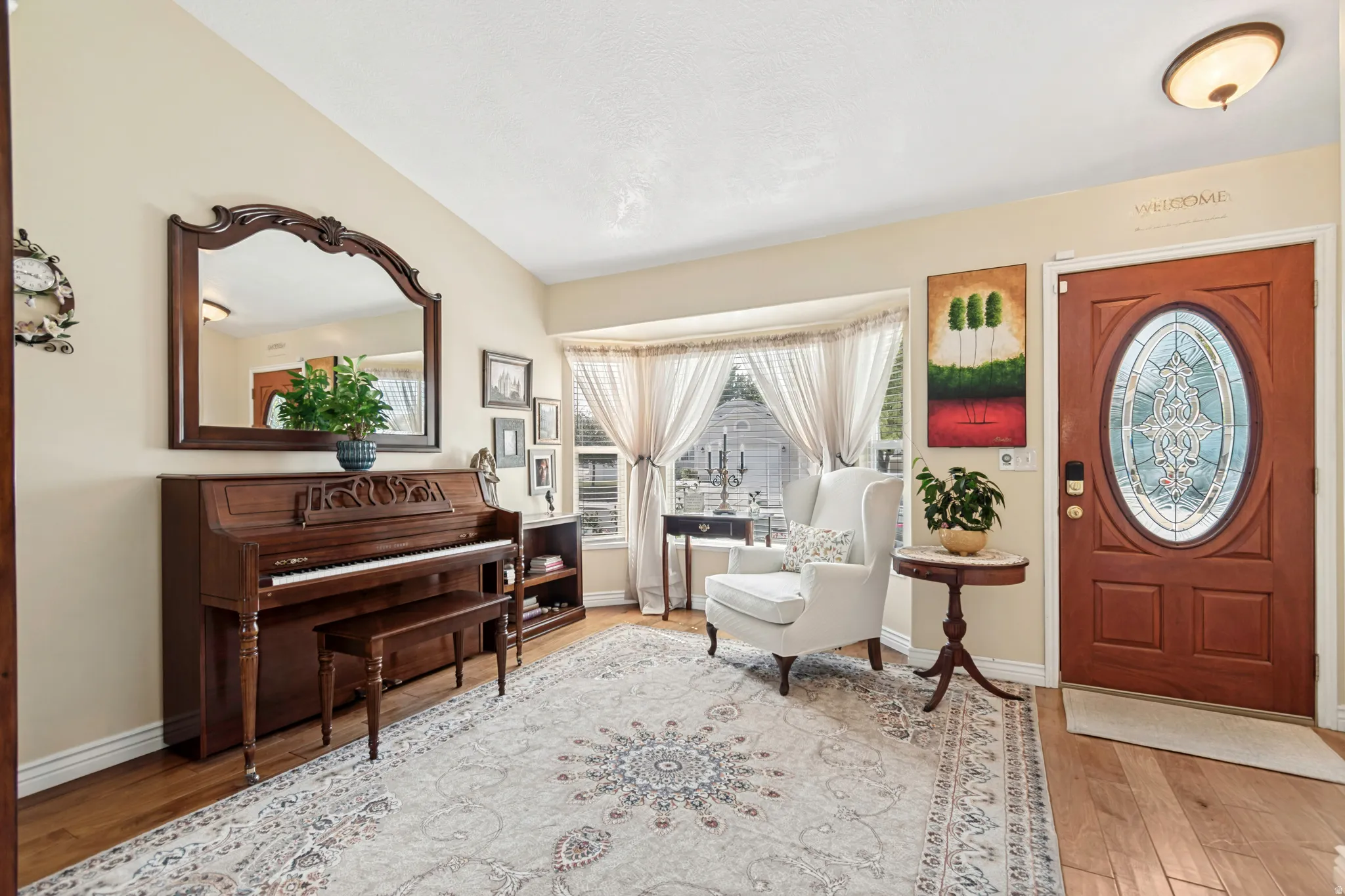 Foyer featuring hardwood flooring, a decorative oval glass-insert door, a large bay window with privacy sheers, and neutral wall tones