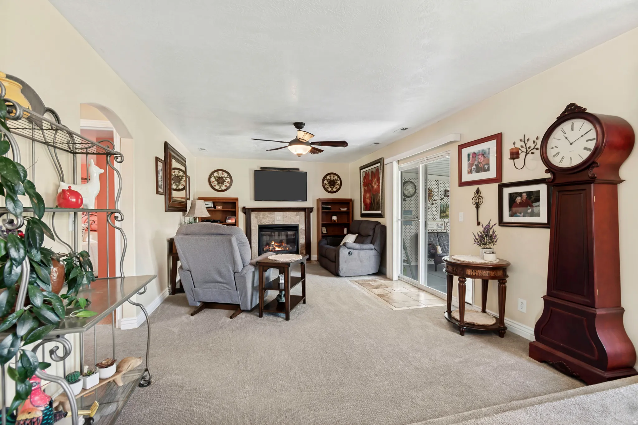 Living area featuring carpet flooring, a fireplace with a stone surround and wood mantle, and a ceiling fan