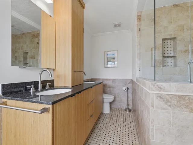 Dual-sink vanity featuring wood-finish cabinetry, dark stone countertops, and contemporary brushed nickel fixtures