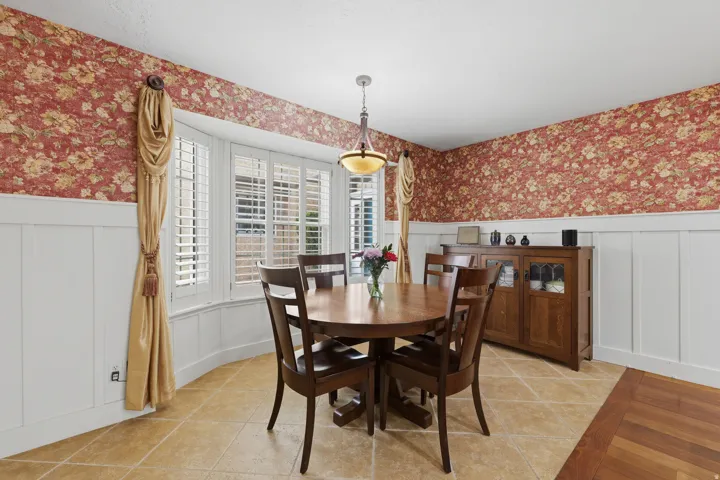 Bay window featuring plantation shutters and draped window treatments, complemented by white wainscoting and floral wallpaper
