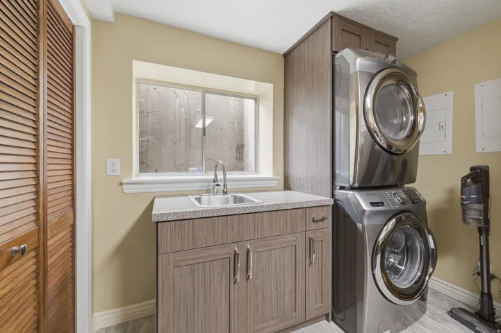 Dedicated utility area featuring a stacked washer and dryer, wood-finish flooring, and a window above a utility sink