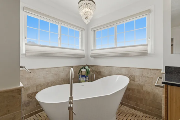 Freestanding soaking tub with floor-mounted faucet, surrounded by tiled walls and hexagonal tile flooring