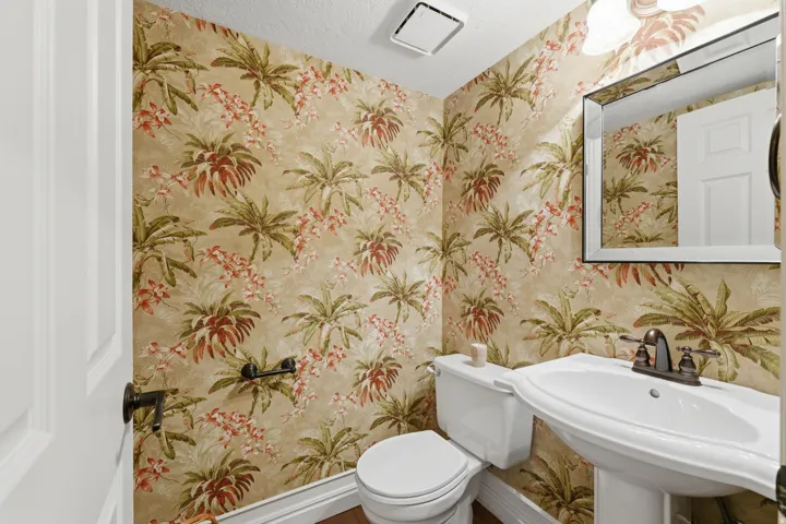 Pedestal sink with bronze-finish faucet, framed wall mirror, and tropical-patterned wallpaper