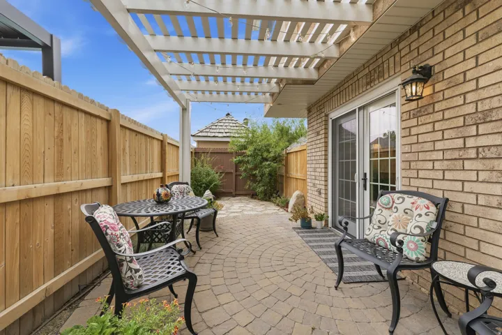 Patio featuring a white pergola, circular paver flooring, privacy fencing, brick exterior, and sliding glass doors