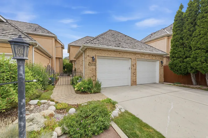 Brick garage facade with two white garage doors, a concrete driveway, and a shingle roof