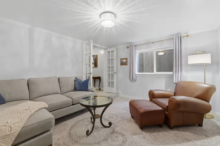 Spacious interior room featuring white walls with crown molding, a decorative ceiling light fixture, a window with natural light, and French doors leading to an additional space