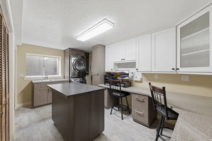 Dedicated laundry and workspace featuring a built-in sink, stackable washer and dryer, extensive cabinetry, and durable countertop surfaces