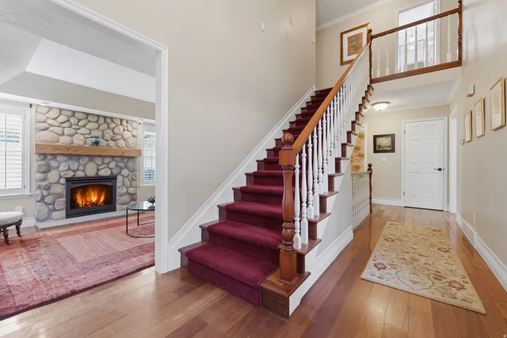 Grand staircase with richly stained wood-finish newel posts and handrails, white balusters, and a plush burgundy runner
