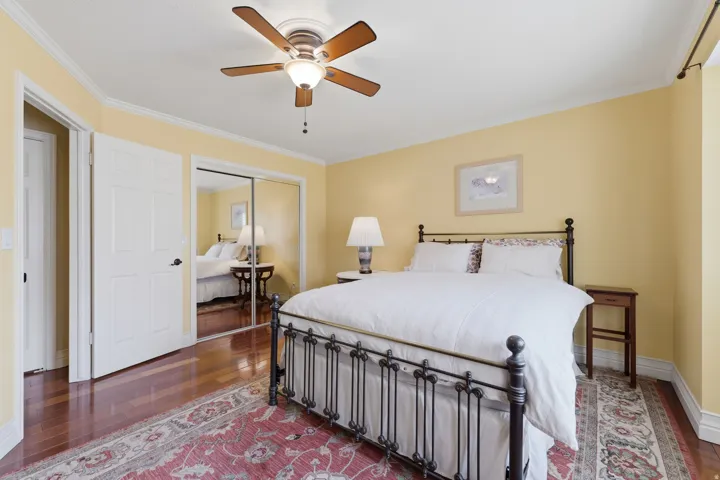 Bedroom featuring wood-finish flooring, ceiling fan with integrated lighting, and mirrored sliding closet doors