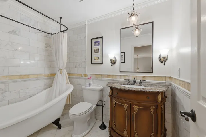 Bathroom featuring a clawfoot tub with shower enclosure, marble-style tile walls, and a decorative vanity with a stone countertop