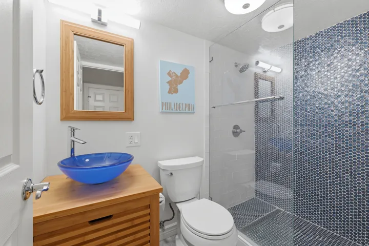 Bathroom featuring a glass-enclosed shower with blue hexagonal tile, a vanity with a blue vessel sink, and a wood-frame mirror