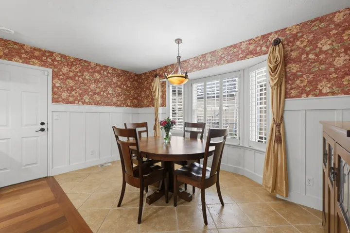 Dining area featuring a bay window with plantation shutters, tile flooring, and wainscoting