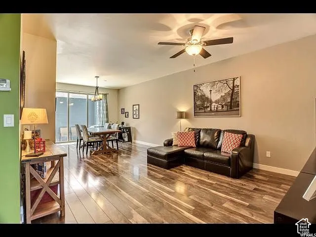 Open-concept living area featuring wood-finish flooring, a ceiling fan with integrated lighting, and neutral wall tones